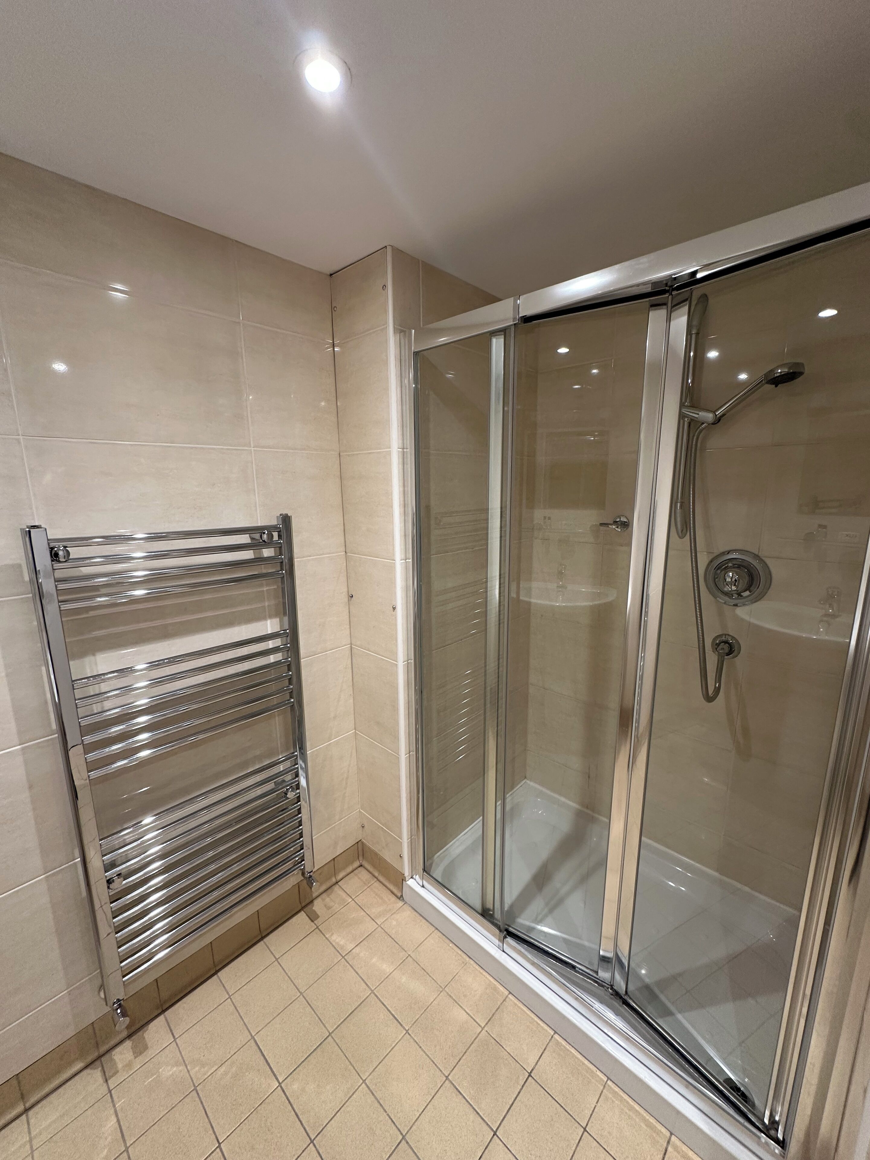 Un baño moderno con ducha envuelta en vidrio, toallero cromado y piso de baldosas.
