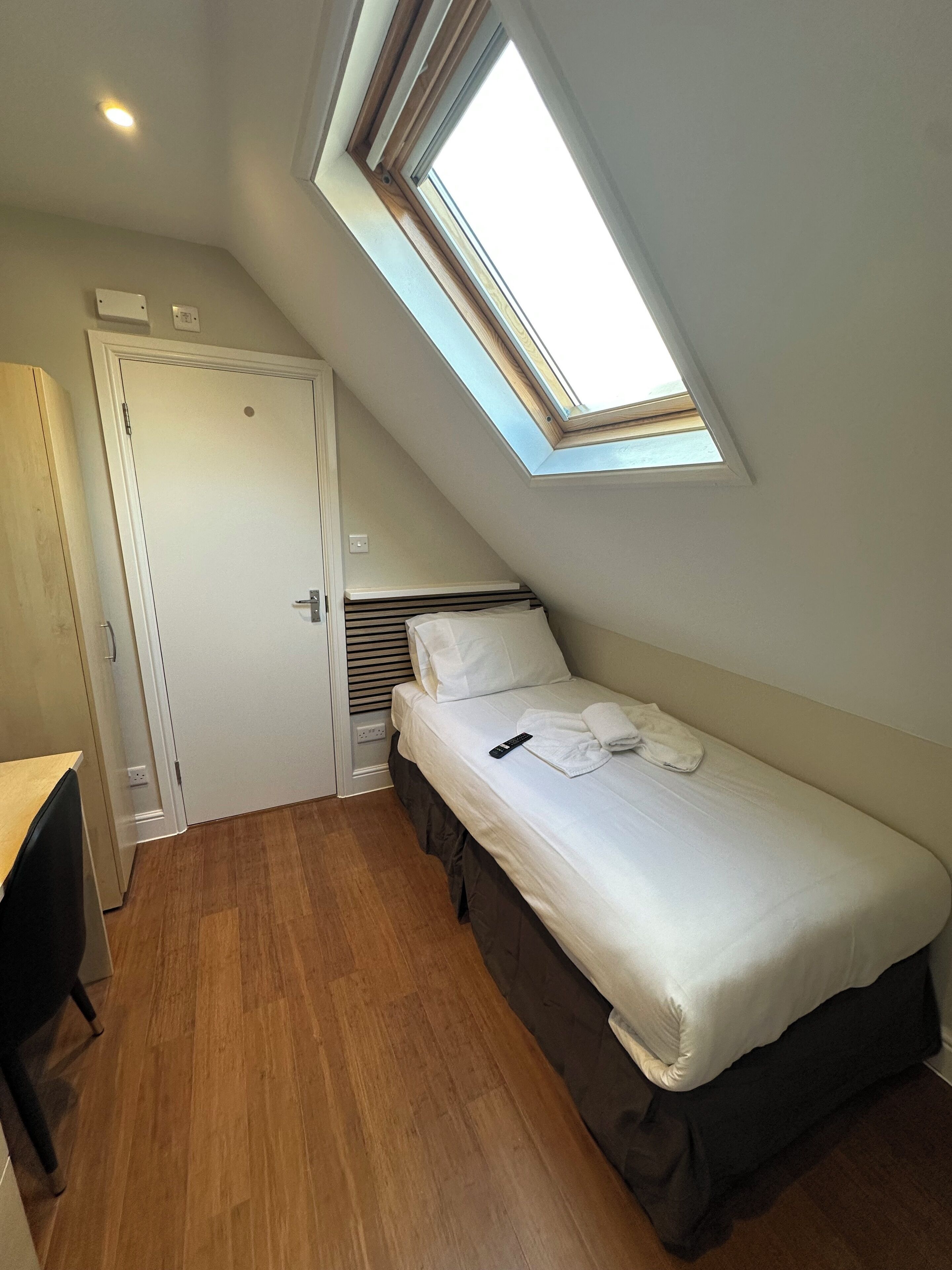 Una habitación pequeña con cama individual, techo inclinado y tragaluz.