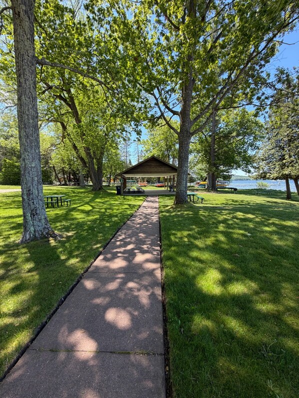A park with a paved walkway, picnic tables, and a covered pavilion.