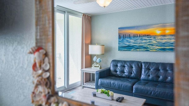 Una sala de estar con un sofá de cuero azul, una mesa de centro, una lámpara y un cuadro con un atardecer sobre el agua.