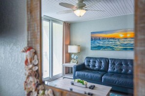 A living room with a blue leather sofa, a coffee table, a lamp, and a painting of a sunset over water. - The Saint Martin Suite | Delightfully Updated Beach Vibes! (Key West)