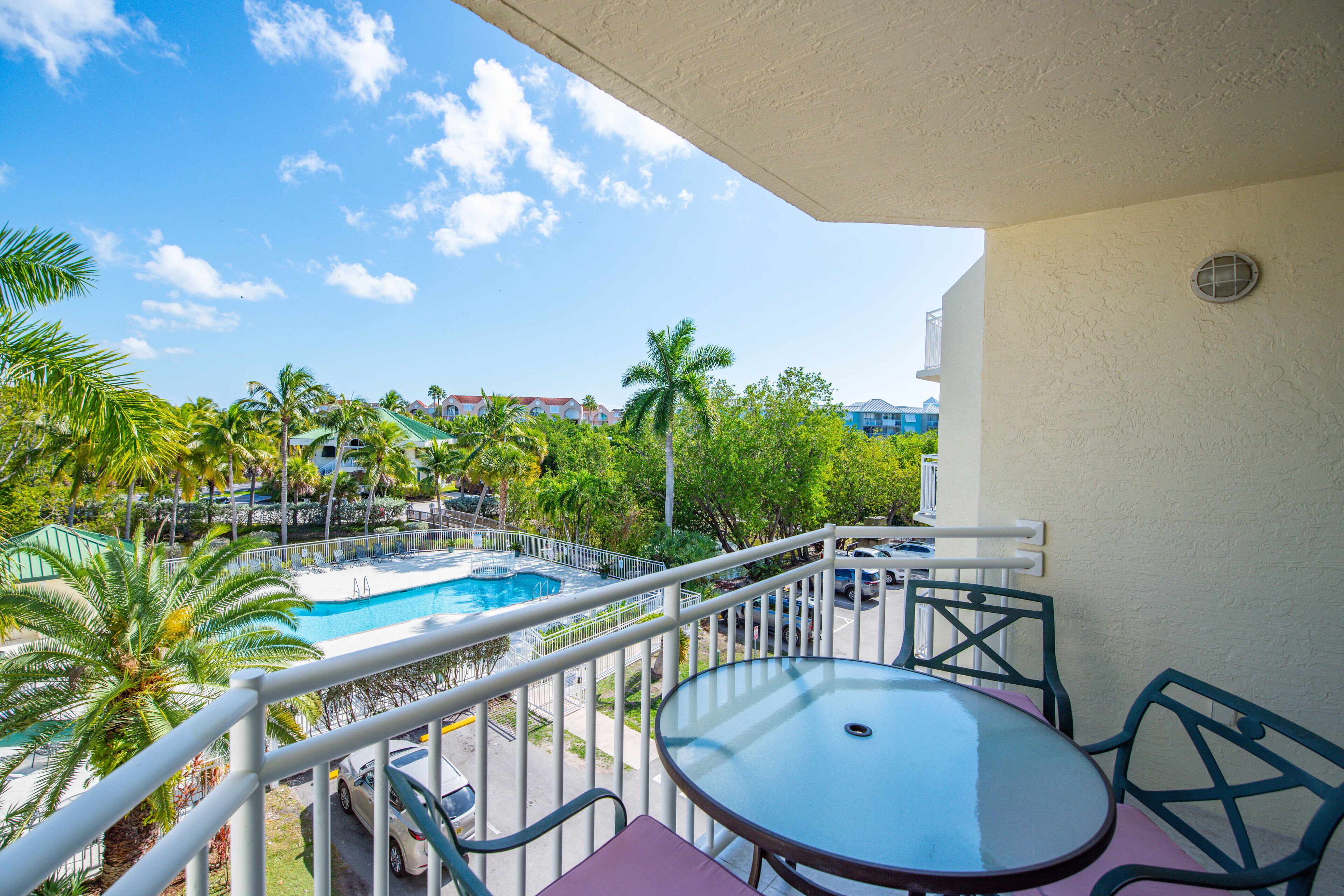 A balcony with a table and chairs, overlooking a swimming pool and palm trees.