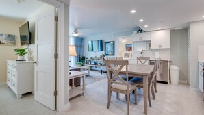 A spacious living area with a dining table, chairs, a sofa, and a TV. There is a kitchen area with cabinets and a dishwasher. - The Grand Cayman | Beautifully Remodeled Key West! (Key West)