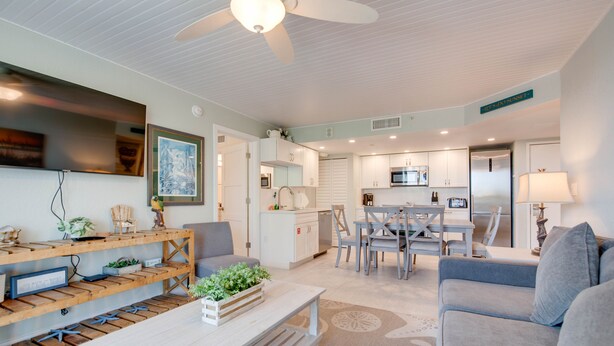 A modern living room with a sofa, coffee table, and a dining area with a table and chairs. There is a kitchen area with cabinets and appliances. - The Grand Cayman | Beautifully Remodeled Key West! (Key West)