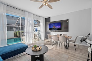 A modern living room with a pool view, a dining area, and a TV on the wall. - Dream Stay|Private Pool & Resort Access| 5min to Parks (Kissimmee)