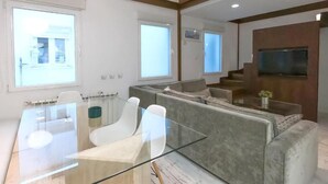 Ein modernes Wohnzimmer mit einem Glastisch, grauem Sofa und einem an der Wand befestigten Fernseher.