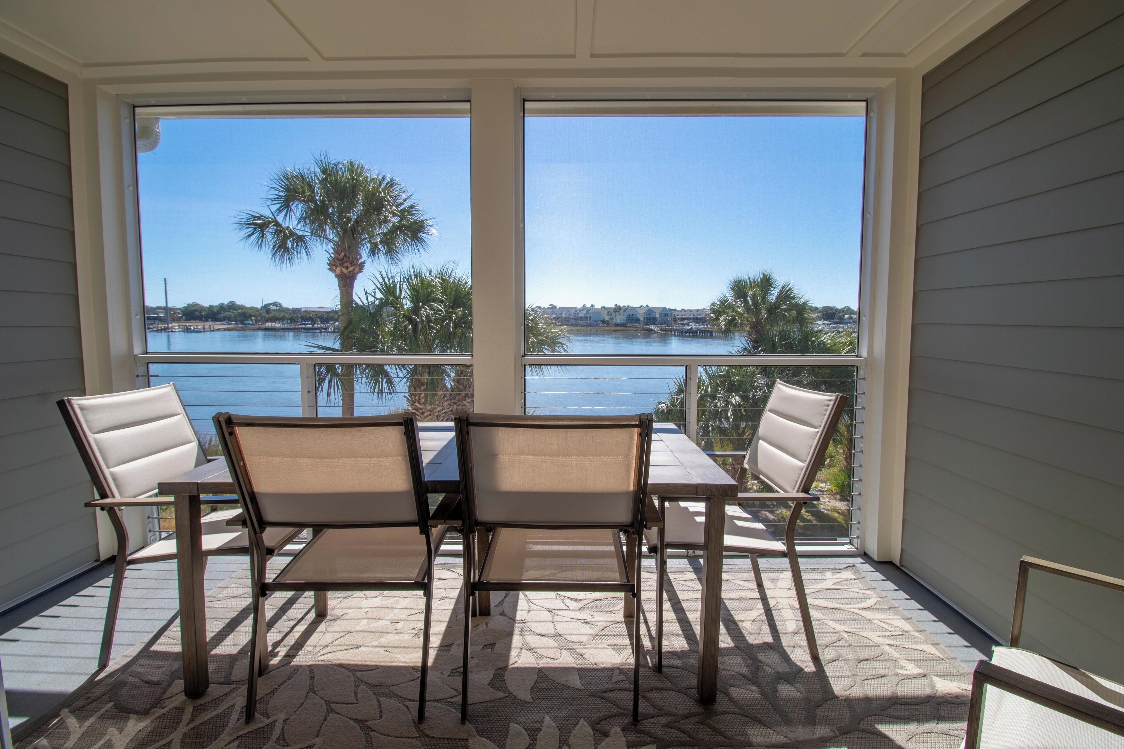 A covered patio with a table and chairs, overlooking a body of water and palm trees.