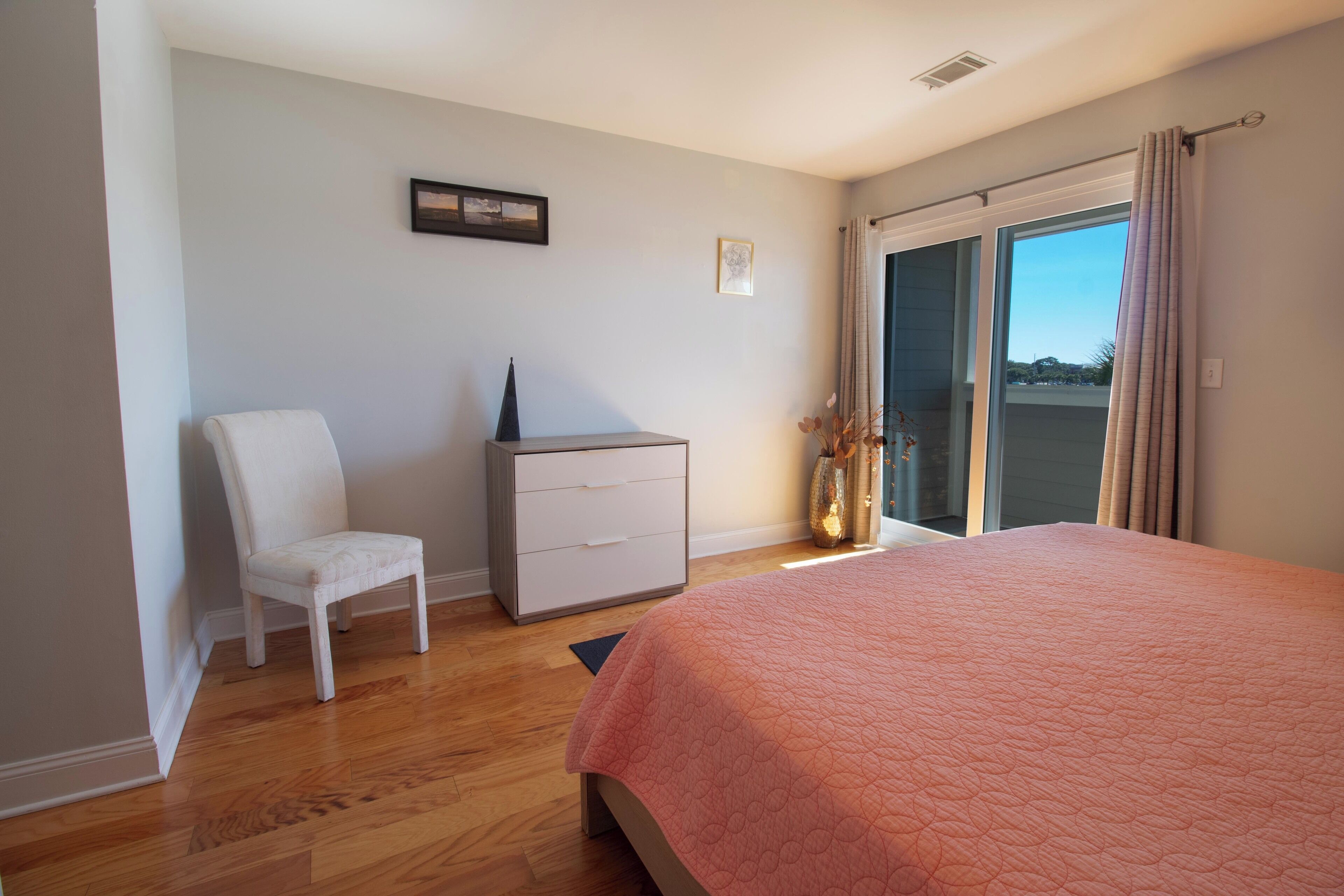 A bedroom with a bed, a chair, a dresser, and a window with curtains.