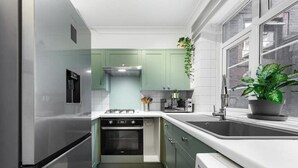 Uma cozinha moderna com armários verdes, uma geladeira de aço inoxidável e um forno embutido.