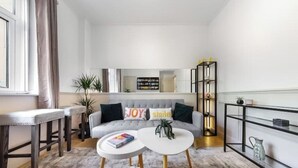Uma sala de estar moderna com um sofá cinzento, duas mesas de centro brancas e uma estante de livros.