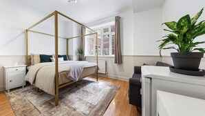 Quarto com uma cama de dossel, mesa de cabeceira, planta em vaso e janela com cortinas.