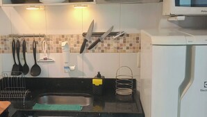 A compact kitchen with a sink, stove, and microwave. There are hanging utensils and a small trash bin. - Crown Casa Copacabana 1 (Rio de Janeiro)