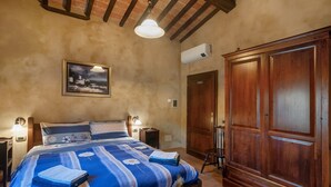 A bedroom with a bed, bedside lamps, a painting, a wardrobe, and an air conditioning unit.