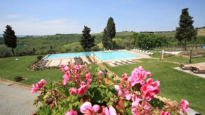 A swimming pool with a deck, surrounded by grass and trees, with a clear sky above.