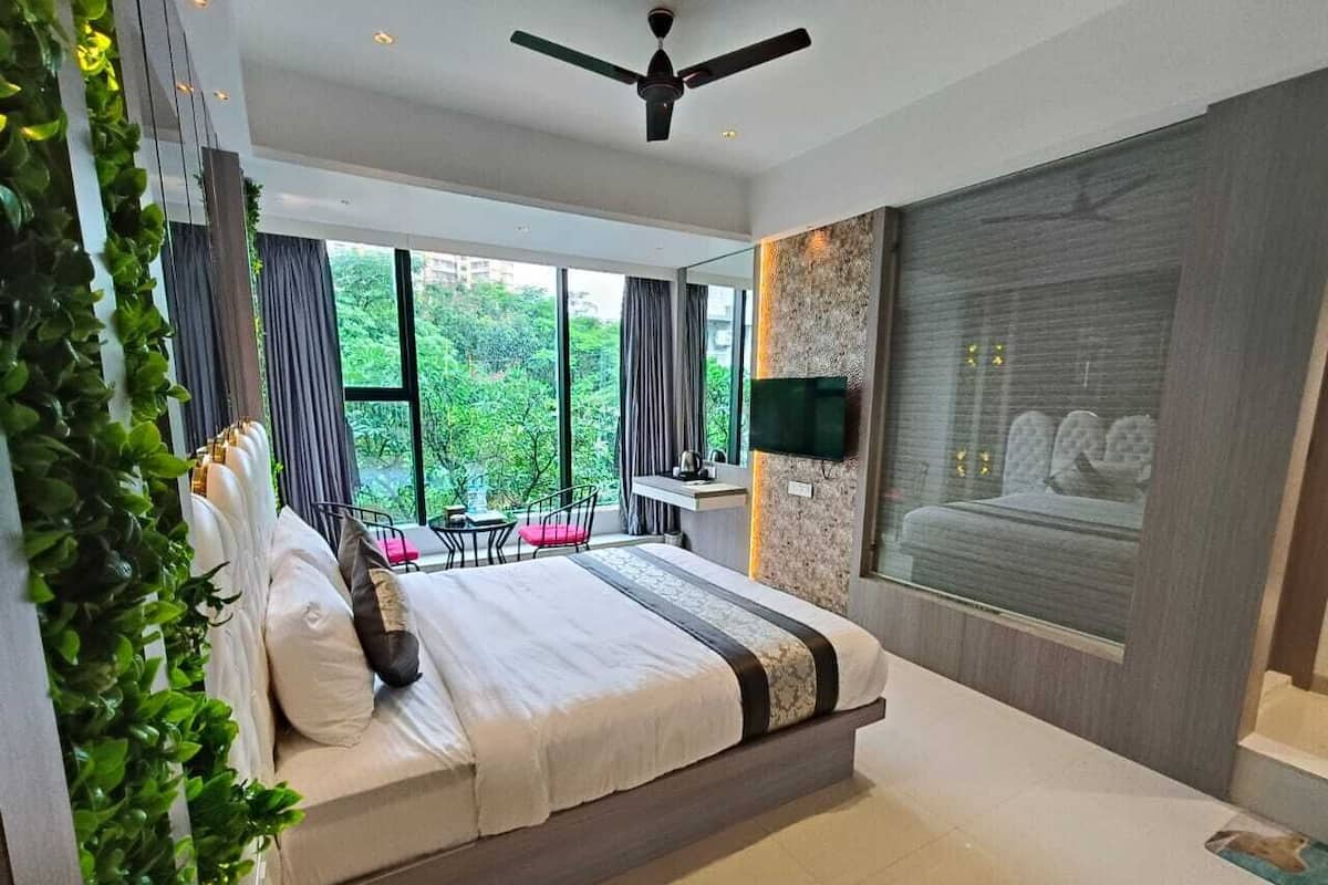 Een moderne slaapkamer met een groot bed, een plafondventilator, een aan de muur bevestigde televisie en uitzicht op groen.