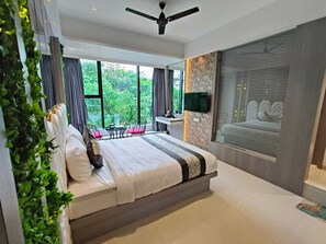 A modern bedroom with a large bed, a ceiling fan, a TV mounted on the wall, and a view of greenery outside. - Melody Boutique Hotel (Thane)