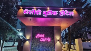 A hotel entrance with a neon sign reading "Hotel Melody" and a water feature in front. - Melody Boutique Hotel (Thane)