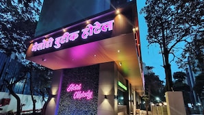 A hotel entrance with a neon sign, a water feature, and a paved walkway. - Melody Boutique Hotel (Thane)