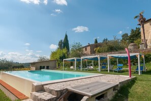 Una piscina amb terrassa de pedra, gandules i una pèrgola amb teulada blava.