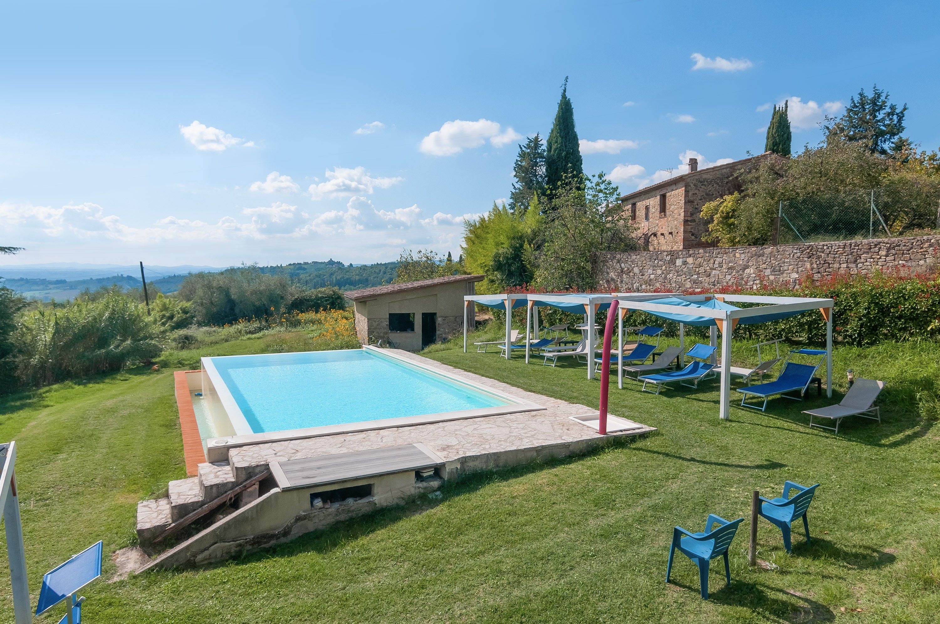 A swimming pool with a stone deck, lounge chairs, and a stone building in the background.