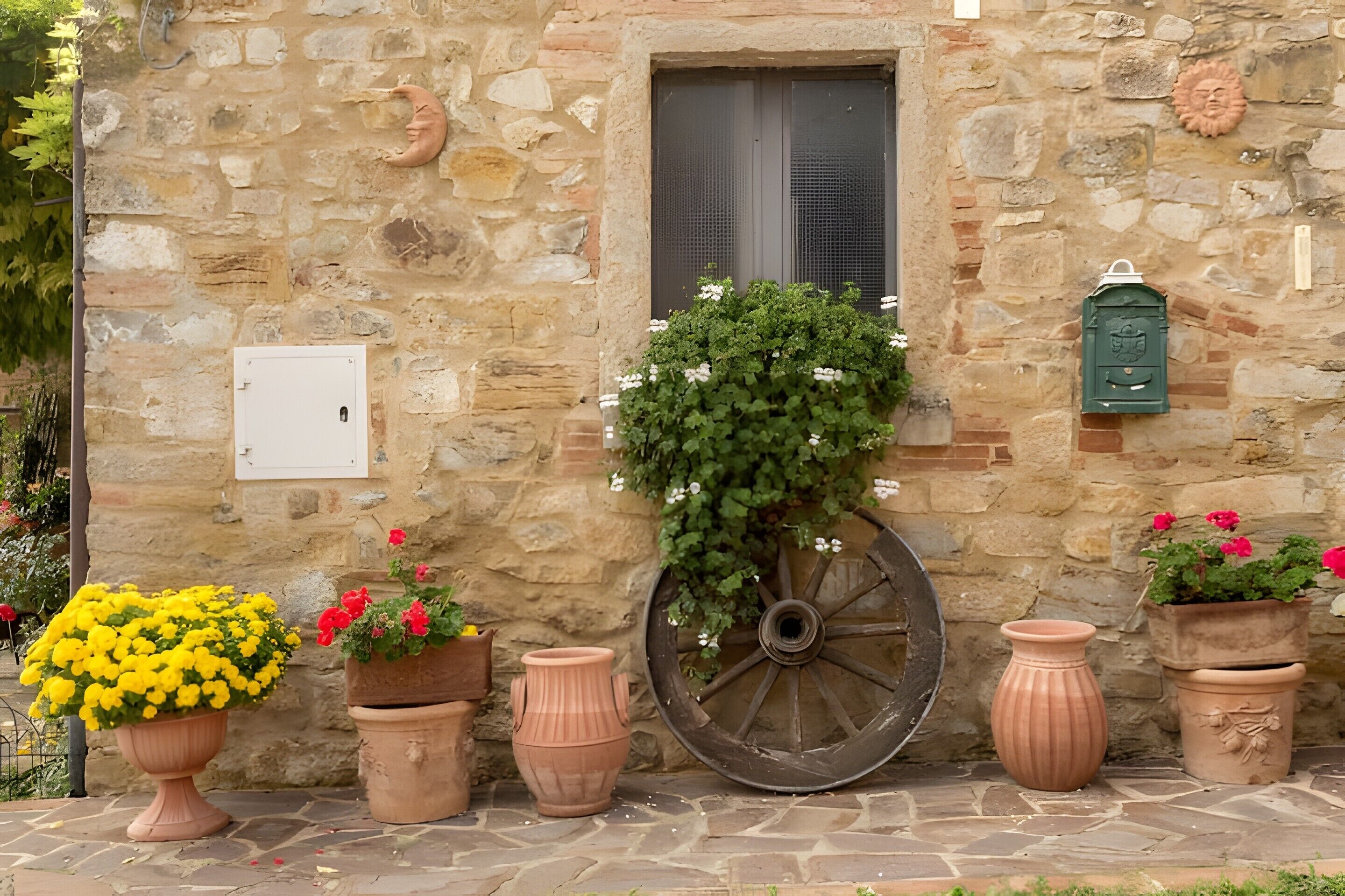 Un bâtiment en pierre doté d’une fenêtre, de plantes en pot et d’une grande roue.