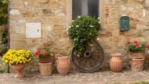 A stone building with a window, potted plants, and a large wheel. - Borghetto di San Filippo Flat with Pool (Barberino Tavarnelle)