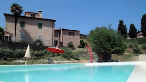 A swimming pool with lounge chairs and a red umbrella, surrounded by greenery and a stone building. - Borghetto di San Filippo Flat with Pool (Barberino Tavarnelle)