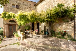 Un edificio in pietra con un patio arredato con sedute all'aperto e piante in vaso.