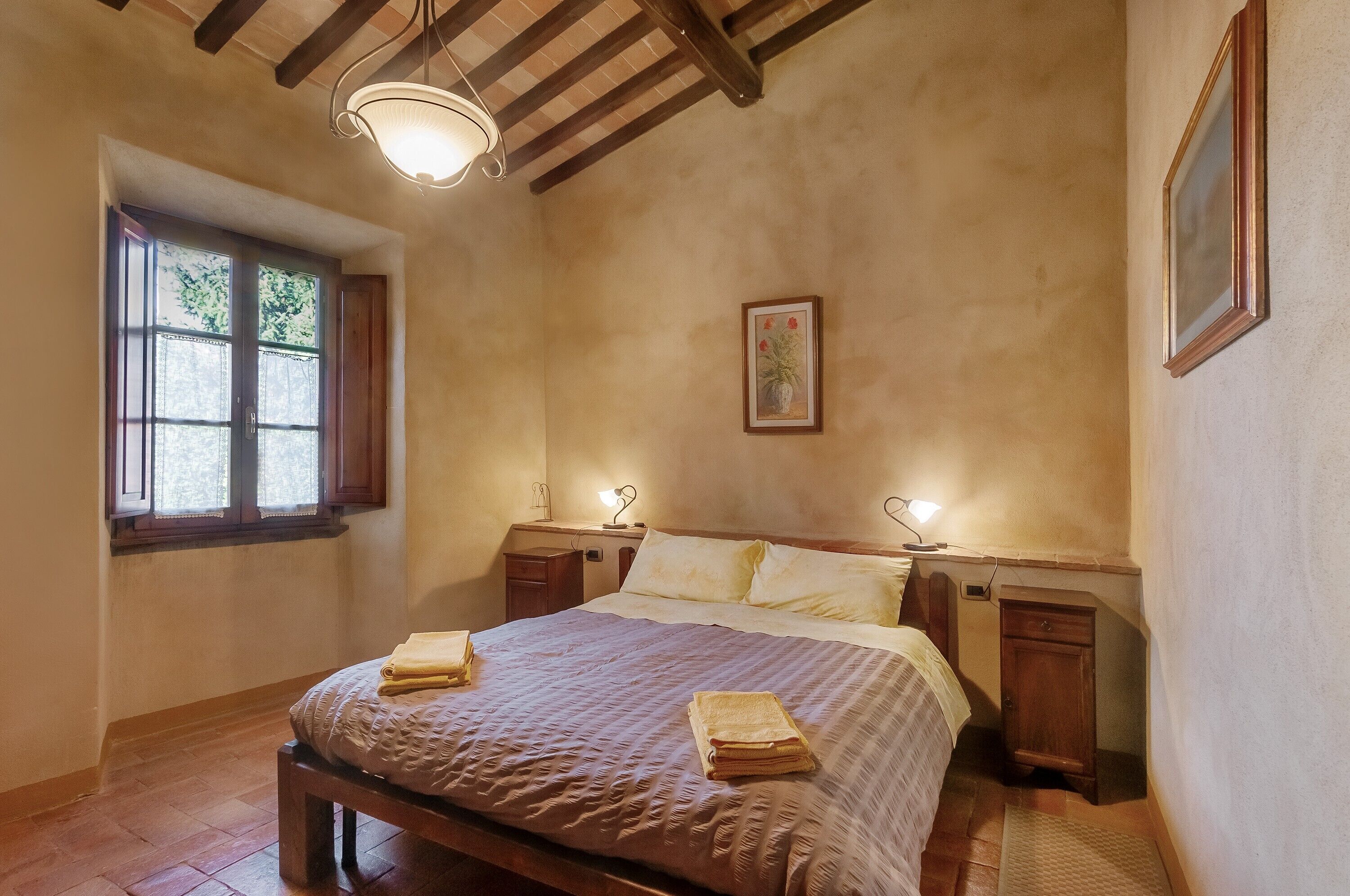 Une chambre à coucher avec un lit, des tables de chevet, une fenêtre et un luminaire au plafond.