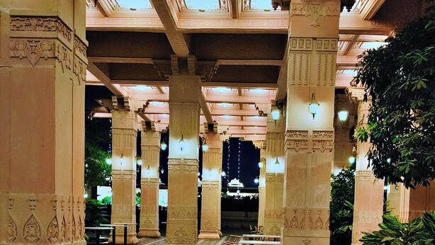 Un'ampia area interna con soffitti alti, colonne decorate e pavimento a motivi. Tavoli e sedie sono disposti per la ristorazione.