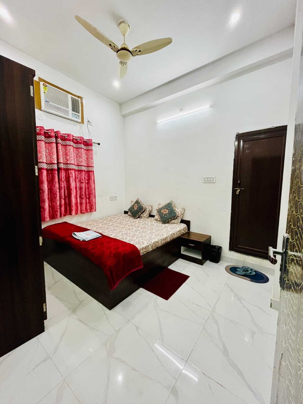 A bedroom with a bed, a ceiling fan, a window with curtains, a door, and a small bedside table.