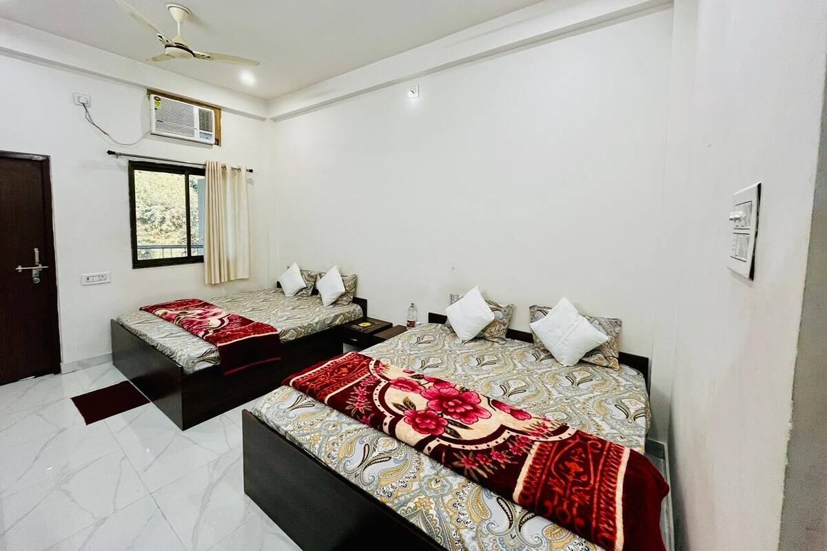 A hotel room with two beds, each with patterned bedding and pillows, a ceiling fan, an air conditioning unit, and a window with curtains.