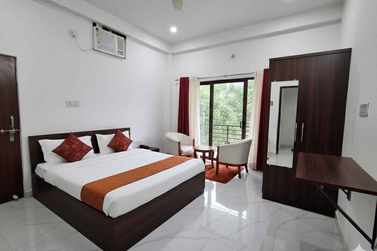 A hotel room with a large bed, a desk, a chair, a balcony with curtains, and a wardrobe.