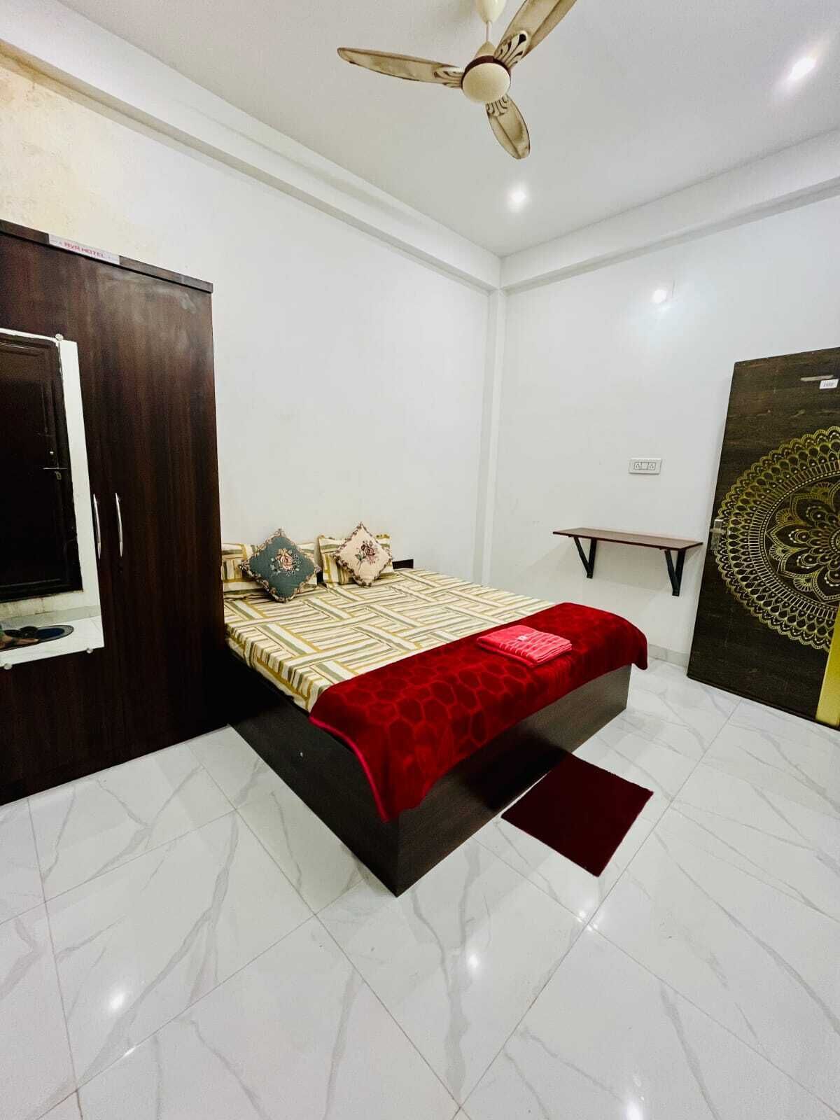 A bedroom with a bed, a wardrobe, a ceiling fan, a wall-mounted TV, and a large decorative wall piece.