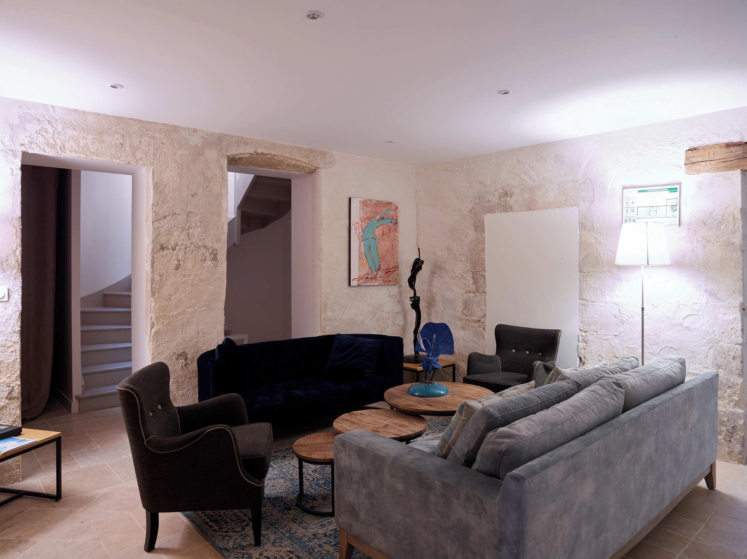 Een woonkamer met een bank, stoelen, een salontafel, een schilderij en een lamp.