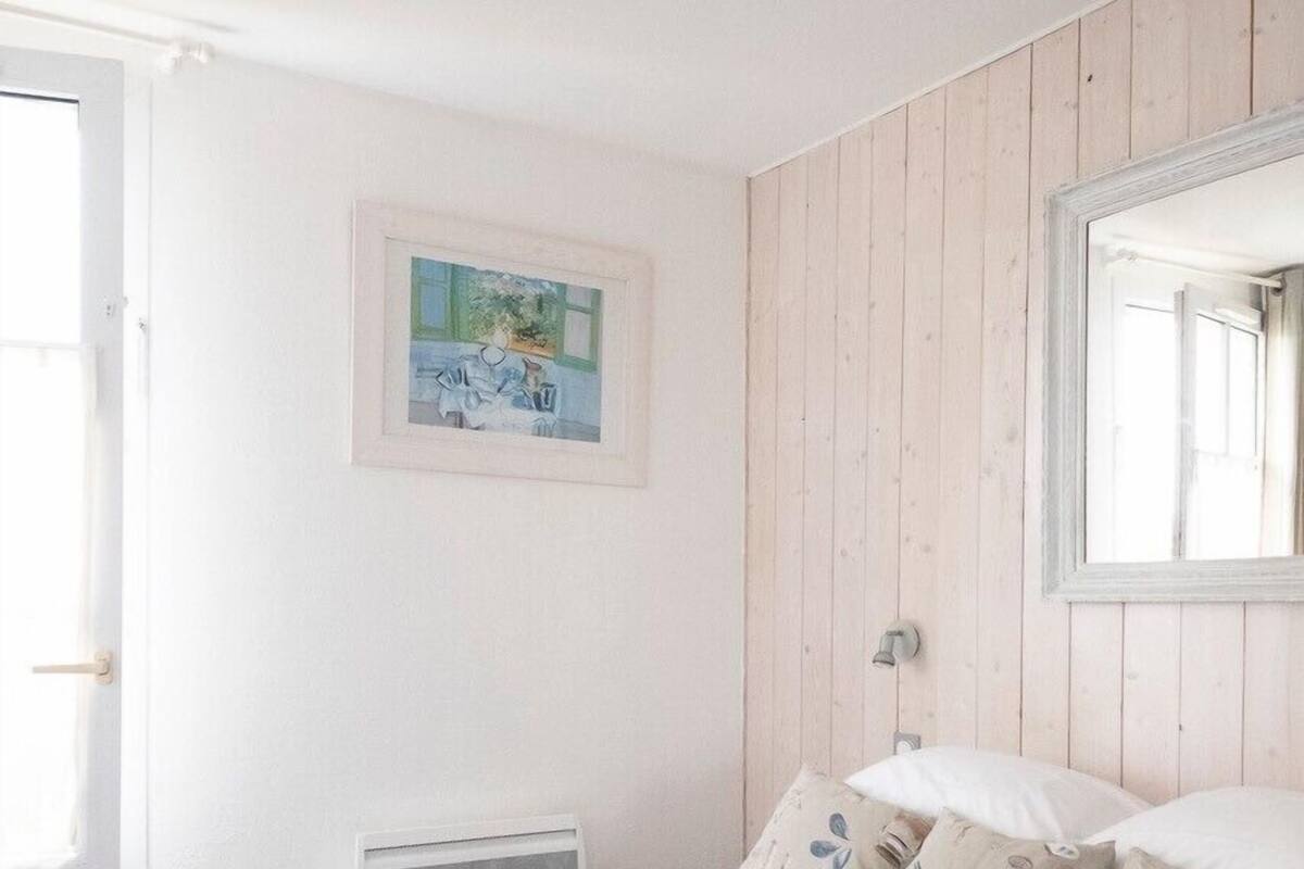Ein Schlafzimmer mit Bett, Fenster, Heizkörper, einem gerahmten Bild und einem Spiegel.