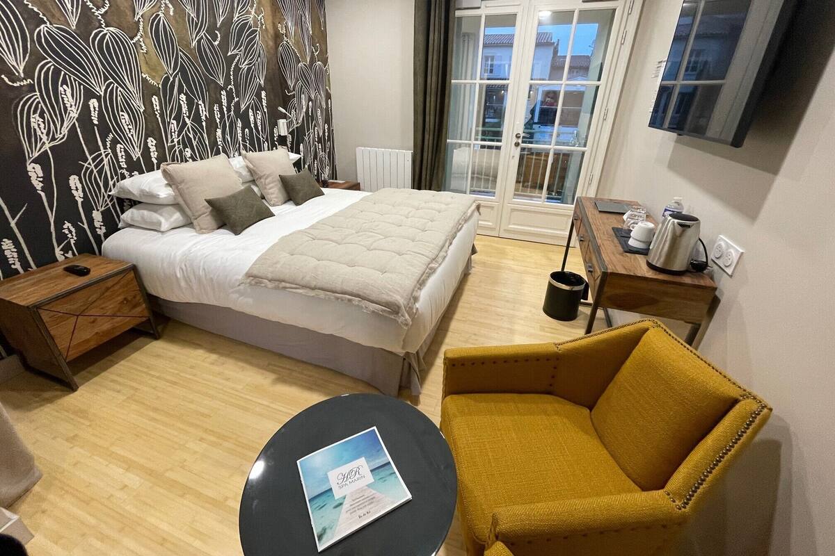 Ein Hotelzimmer mit Bett, Sessel, Tisch, Fernseher und Fenster mit Blick, sowie einer Wand mit Muster.