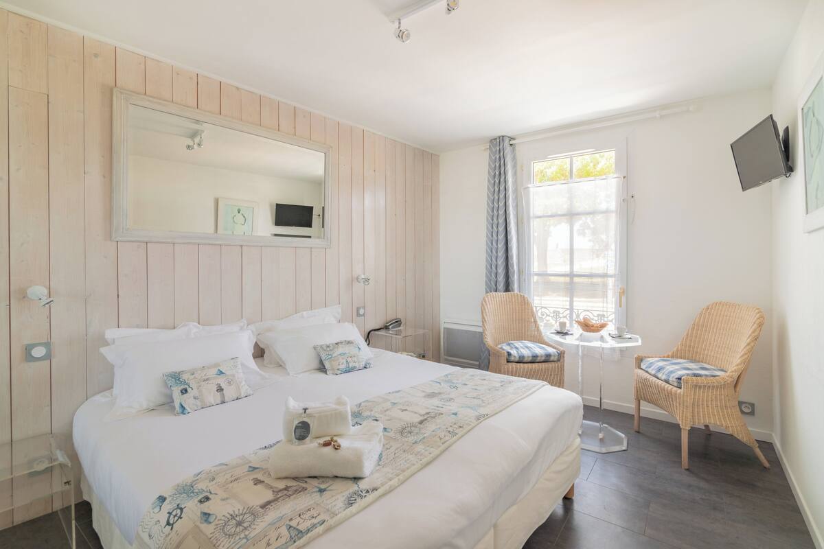 Ein Hotelzimmer mit Bett, Stuhl, kleinem Tisch, Fernseher und einem Fenster mit Vorhängen.