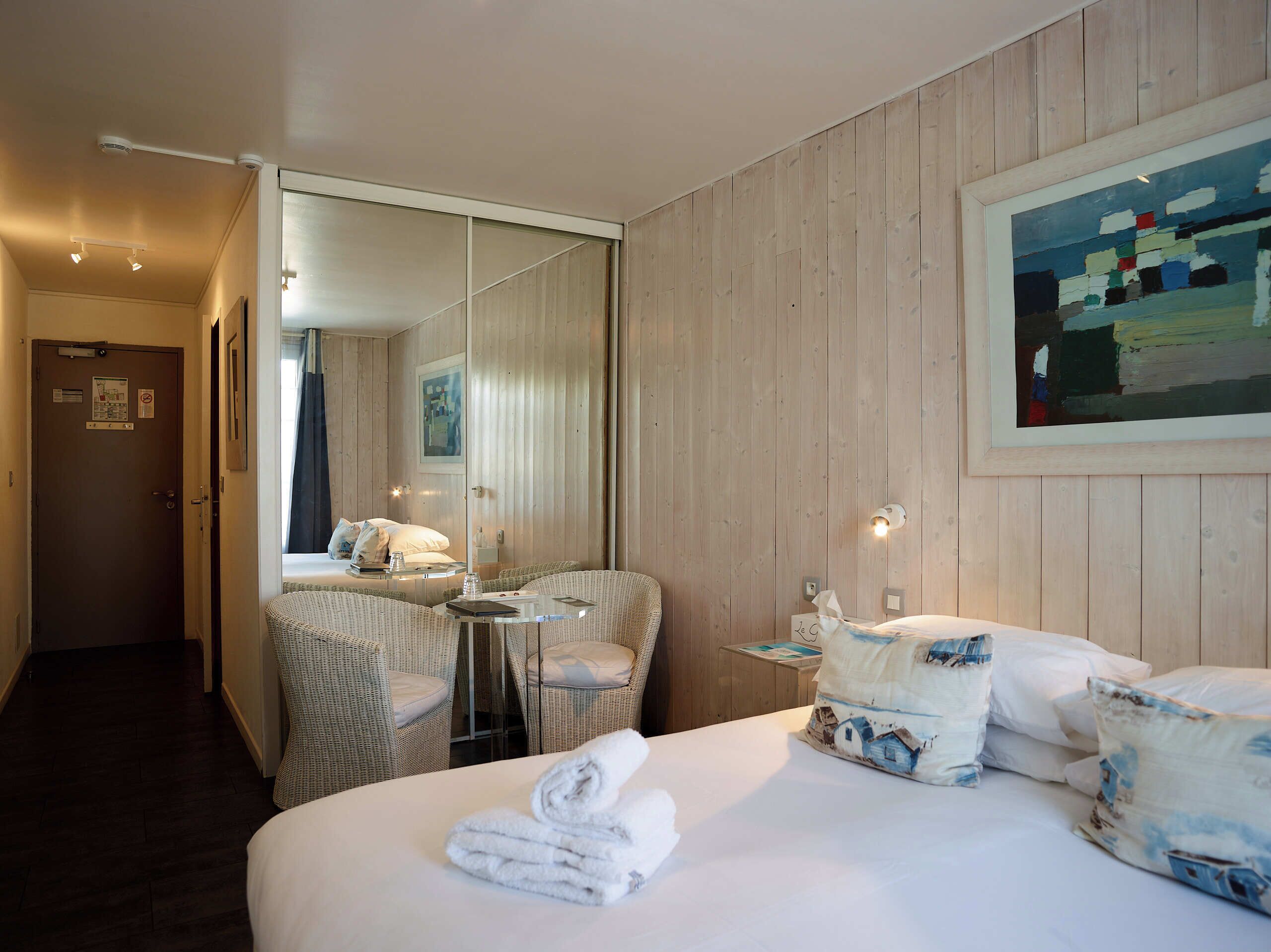 Een hotelkamer met een bed, een stoel, een tafeltje, een spiegel en een schilderij aan de muur.