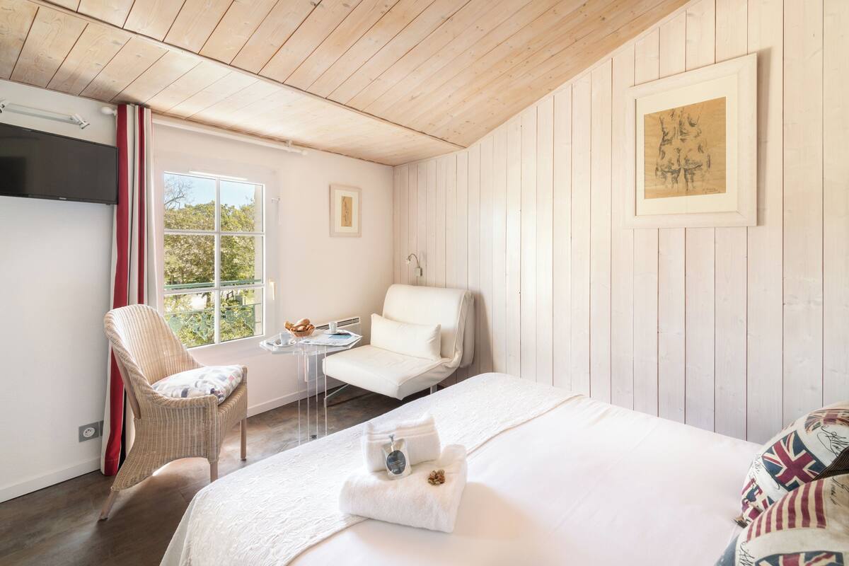 Ein Zimmer mit einem Bett, einem Sessel, einem kleinen Tisch und einem Fenster.