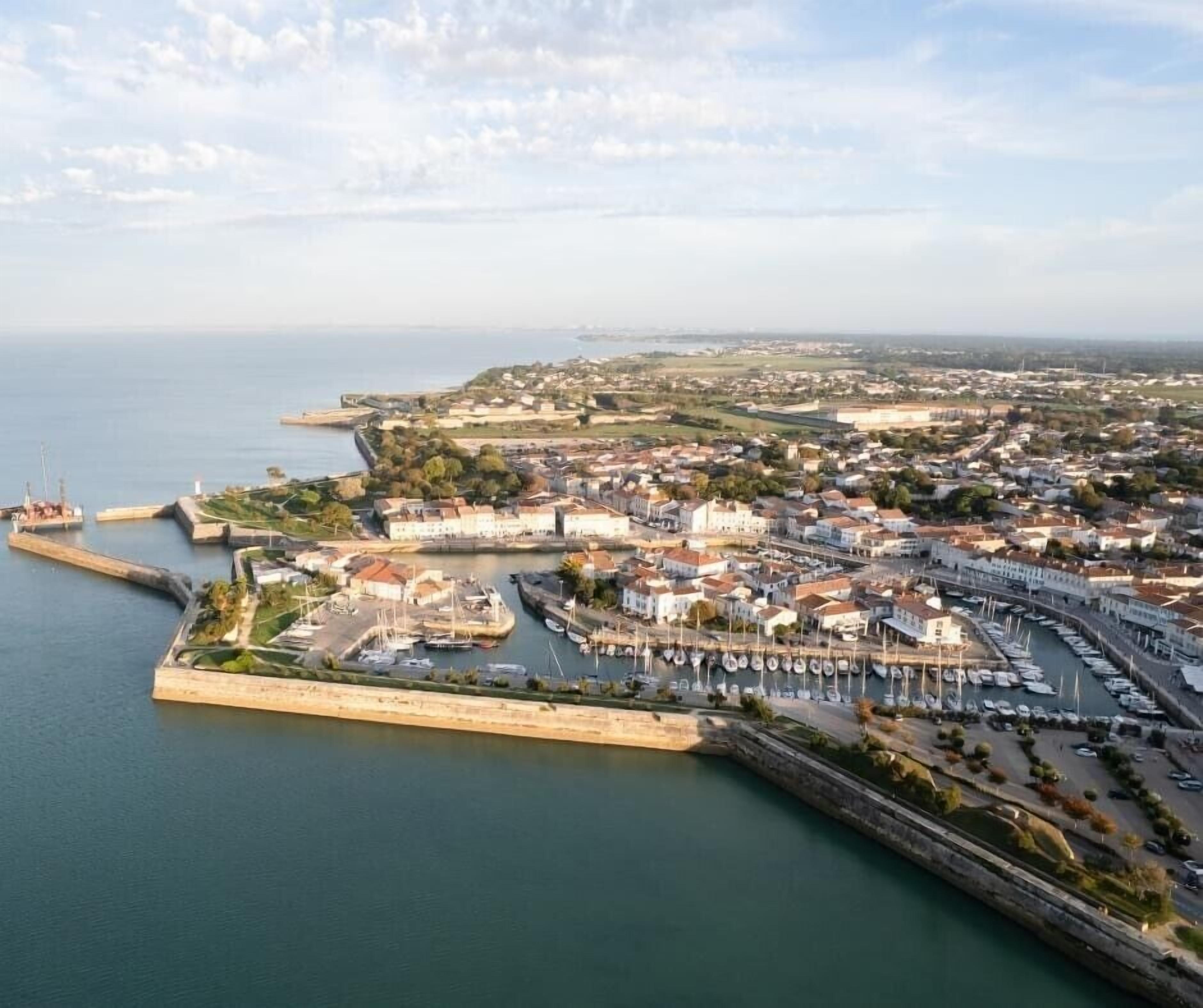 An aerial view of a coastal town with a marina, buildings, and a fortified wall.