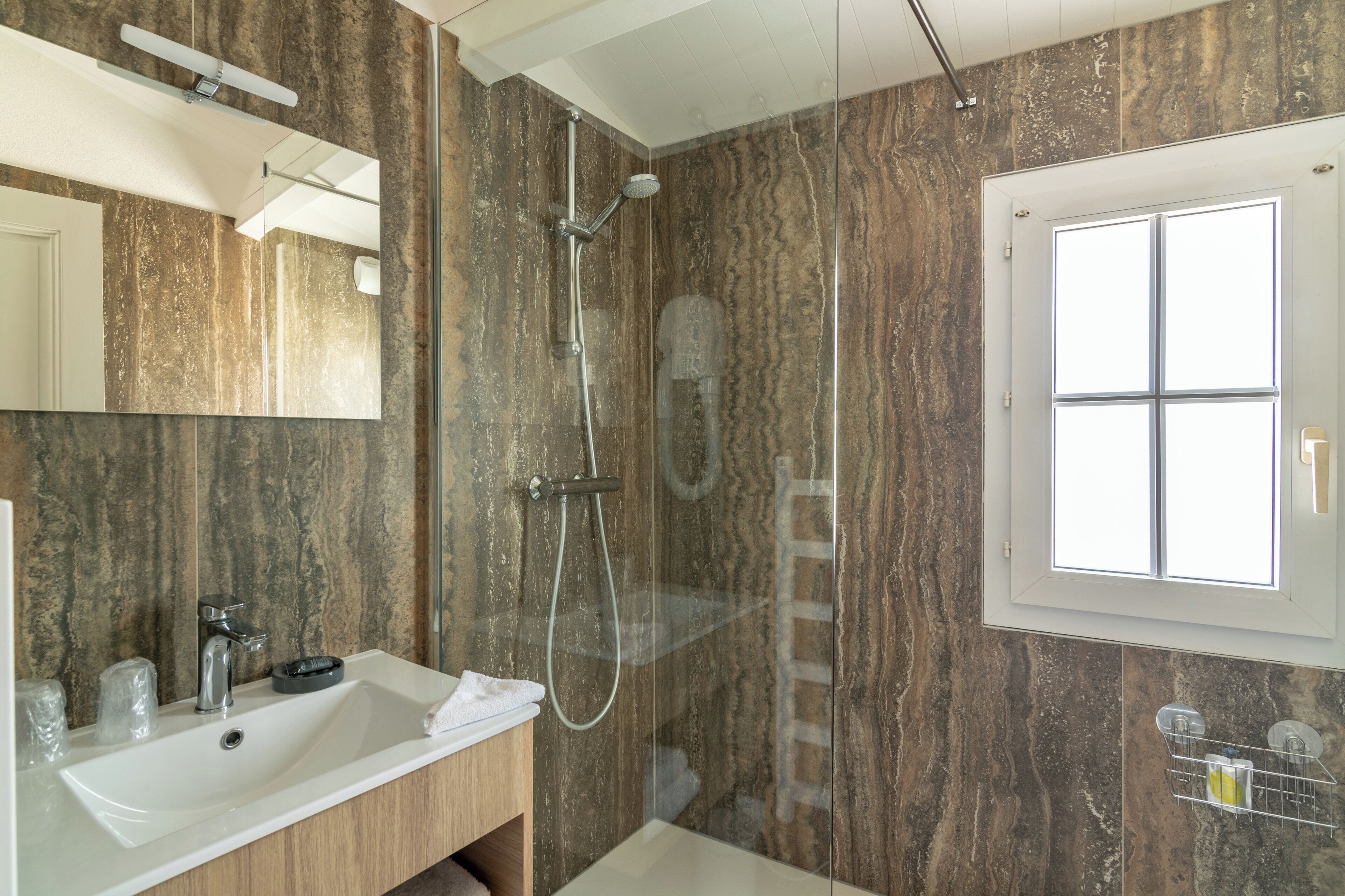 Un baño moderno con pared de mármol, un espejo grande, un lavamanos y una ducha.