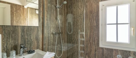 Un baño moderno con pared de mármol, un espejo grande, un lavamanos y una ducha.