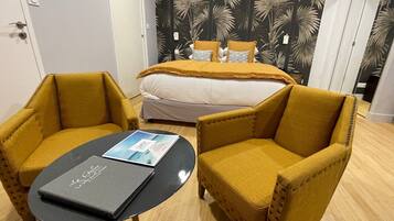 Habitación de hotel con cama, dos sillones amarillos, una mesita con una revista y un papel tapiz tropical.