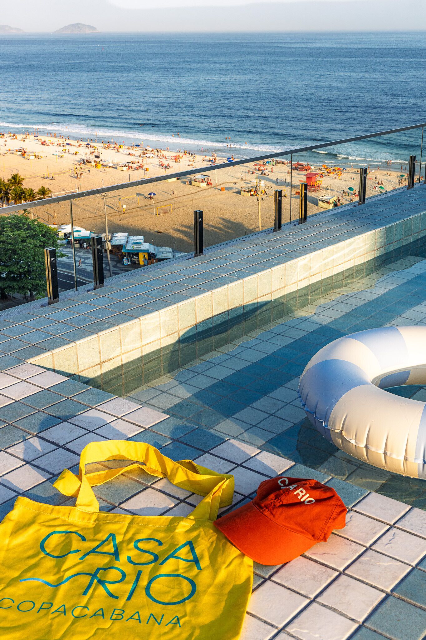 A poolside view with a beach in the background, a yellow bag, and a red cap.