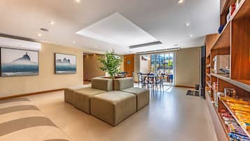 A modern hotel lobby with a seating area, a bookshelf, and a view of the outside.