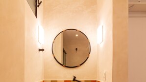 Un baño con un espejo redondo, un lavamanos blanco y un salpicadero de azulejos.