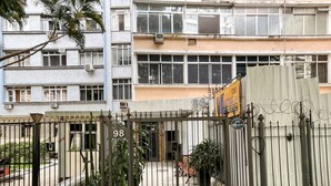 Una entrada protegida por una reja a un edificio, con el número '98' y un letrero de servicio las 24 horas.