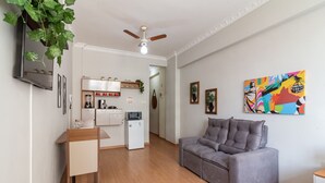 Una sala moderna con un sofá gris, una mesa de comedor de madera y una cocina al fondo.