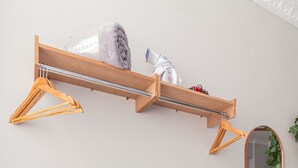 Un banco de madera con estructura metálica, un estante de madera con perchas y un espejo en la pared.